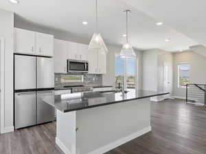 Kitchen featuring dark hardwood / wood-style flooring, sink, white cabinets, a kitchen island with sink, and appliances with stainless steel finishes