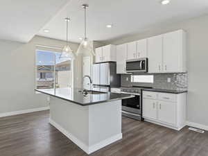 Kitchen featuring dark hardwood / wood-style floors, stainless steel appliances, a center island with sink, sink, and white cabinets