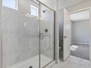 Bathroom featuring a wealth of natural light, an enclosed shower, toilet, and tile floors