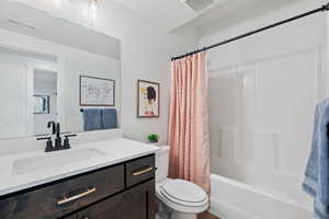 Full bathroom with a textured ceiling, shower / tub combo with curtain, vanity, and toilet