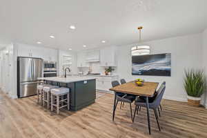 Kitchen featuring white cabinets, a center island with sink, appliances with stainless steel finishes, and light hardwood / wood-style flooring