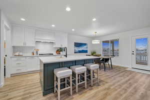 Kitchen featuring stainless steel gas cooktop, light hardwood / wood-style floors, a kitchen island with sink, and white cabinetry