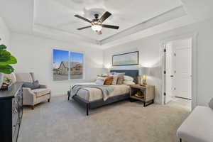 Carpeted bedroom featuring a tray ceiling and ceiling fan