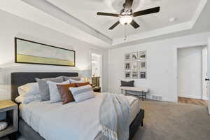 Bedroom featuring wood-type flooring, a tray ceiling, ensuite bathroom, and ceiling fan