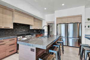 Kitchen featuring stainless steel appliances, a kitchen breakfast bar, tasteful backsplash, a kitchen island with sink, and sink