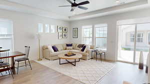 Living room featuring a raised ceiling, ceiling fan, and light wood-type flooring