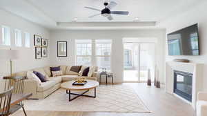 Living room featuring a tray ceiling, light wood-type flooring, fireplace, and ceiling fan