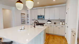 Kitchen featuring decorative light fixtures, a center island with sink, tasteful backsplash, light wood-type flooring, and white cabinets