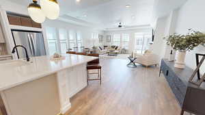 Kitchen with large island, light wood-type flooring, a tray ceiling, stainless steel refrigerator, sink, and ceiling fan