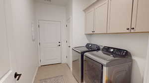 Clothes washing area with cabinets, light tile floors, and upper cabinets