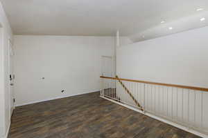 Empty room with vaulted ceiling, a textured ceiling, and dark wood-type flooring