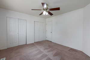 Unfurnished bedroom featuring two closets, ceiling fan, and carpet floors