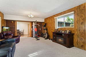 Carpeted living room featuring wooden walls, a textured ceiling, and a chandelier