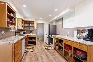 Kitchen featuring light stone counters, light hardwood / wood-style floors, backsplash, range with electric cooktop, and stainless steel fridge