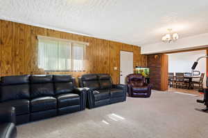 Living room with carpet, an inviting chandelier, a textured ceiling, and wood walls