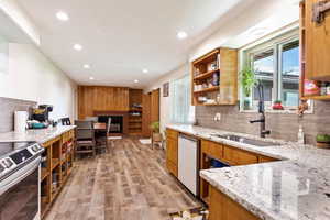 Kitchen featuring tasteful backsplash, dishwashing machine, light wood-type flooring, stainless steel electric stove, and sink