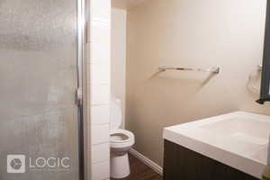 Bathroom featuring a shower with door, hardwood / wood-style flooring, toilet, and vanity