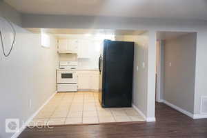 Kitchen with black fridge, white cabinets, stove, and light tile floors