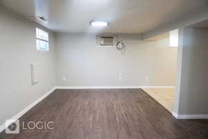 Basement with a wall unit AC and hardwood / wood-style flooring