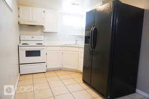 Kitchen with white cabinets, light tile floors, white electric range oven, and black fridge with ice dispenser