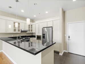 Kitchen with kitchen peninsula, decorative light fixtures, white cabinets, dark tile floors, and appliances with stainless steel finishes