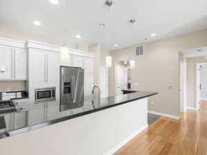 Kitchen with light hardwood / wood-style floors, white cabinetry, dark stone countertops, appliances with stainless steel finishes, and decorative light fixtures