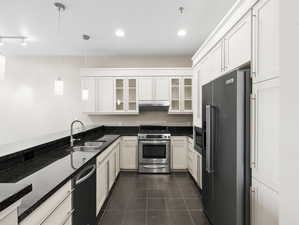 Kitchen with stainless steel appliances, white cabinets, decorative light fixtures, sink, and dark tile flooring