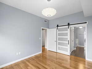 Unfurnished bedroom featuring a barn door and hardwood / wood-style floors