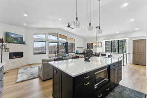 Kitchen with light stone counters, a kitchen island, built in microwave, decorative light fixtures, and vaulted ceiling