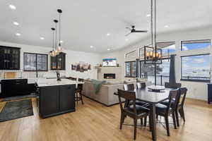 Dining area with lofted ceiling, a stone fireplace, ceiling fan, and light wood-type flooring