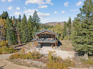 Rear view of house with driveway, a deck with mountain view, a garage, and a forest view