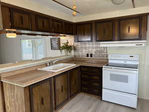 Kitchen featuring light hardwood / wood-style flooring, dark brown cabinets, backsplash, white range with electric stovetop, and sink