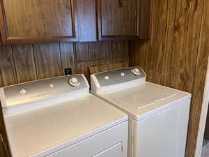 Clothes washing area with cabinets, wooden walls, and washing machine and clothes dryer