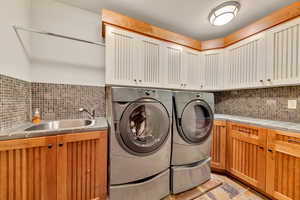 Laundry room featuring cabinets, sink, separate washer and dryer, and light tile flooring