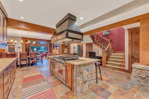 Kitchen with custom range hood, high end stove, decorative light fixtures, a breakfast bar, and light tile floors