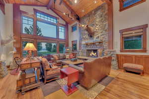 Living room with a stone fireplace, high vaulted ceiling, light hardwood / wood-style floors, and wooden ceiling