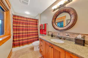 Full bathroom featuring tile floors, shower / tub combo with curtain, backsplash, vanity, and toilet