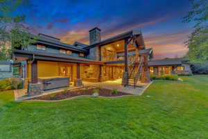 Back house at dusk featuring a patio area and a lawn