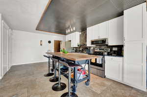 Kitchen with appliances with stainless steel finishes, white cabinetry, light tile floors, and wooden counters