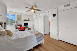 Bedroom featuring two closets, ceiling fan, a textured ceiling, and light wood-type flooring