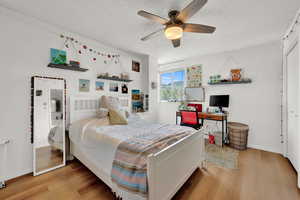 Bedroom with a textured ceiling, ceiling fan, a closet, and hardwood / wood-style floors