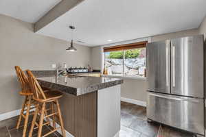 Kitchen with dark tile floors, hanging light fixtures, a kitchen bar, stainless steel fridge, and sink