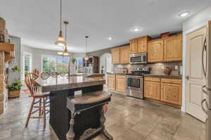 Kitchen featuring a breakfast bar area, stainless steel appliances, backsplash, and light tile floors