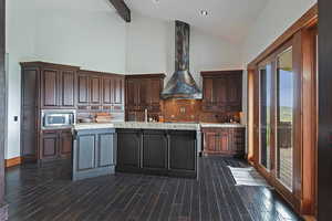 Kitchen with a center island with sink, appliances with stainless steel finishes, wall chimney exhaust hood, high vaulted ceiling, and tasteful backsplash