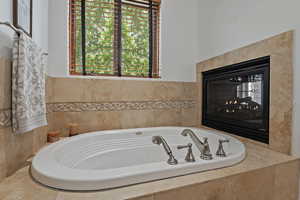 Bathroom featuring a multi sided fireplace and tiled tub