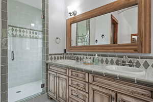 Bathroom featuring a shower with door, tasteful backsplash, and double vanity