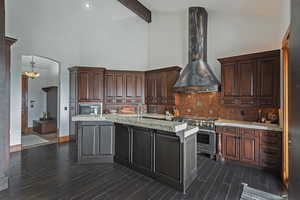 Kitchen featuring an island with sink, wall chimney exhaust hood, stainless steel appliances, and high vaulted ceiling