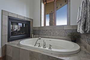 Bathroom featuring a relaxing tiled bath and a multi sided fireplace