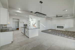 Kitchen with an island with sink, decorative light fixtures, white cabinetry, and light tile floors