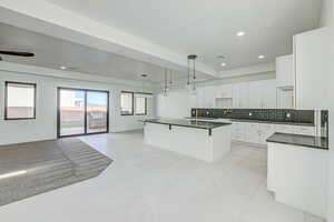 Kitchen with an island with sink, pendant lighting, backsplash, light tile floors, and white cabinetry